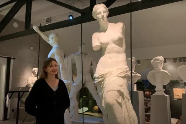 Svartklädd kvinna står i en sal med vita antika skulpturer.